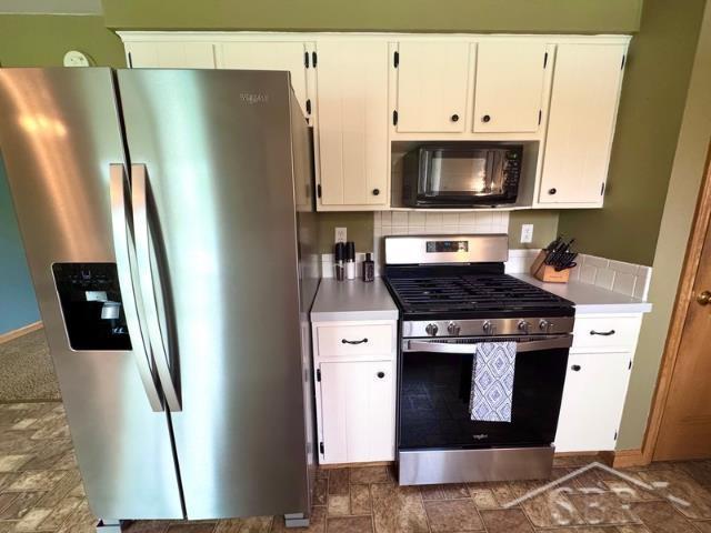 7200 Danny Dr, Saginaw, MI 48609 - kitchen featuring stainless steel appliances, white cabinets, light countertops, stone finish flooring, and tasteful backsplash