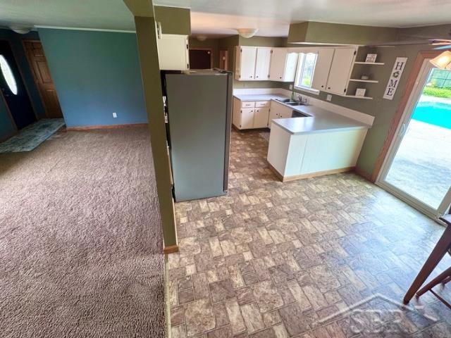 7200 Danny Dr, Saginaw, MI 48609 - kitchen with freestanding refrigerator, white cabinets, a sink, a peninsula, and open shelves