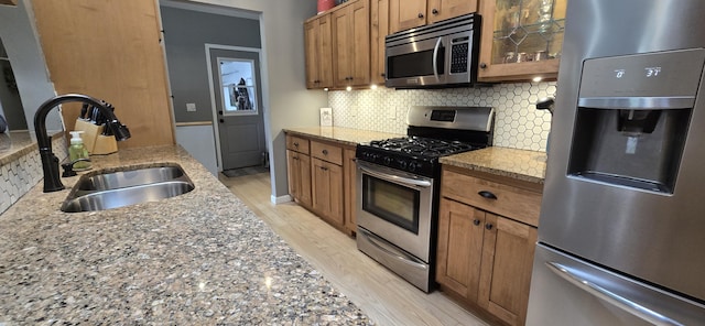 4447 Deer Creek Dr, Norton Shores, MI 49441 - kitchen featuring appliances with stainless steel finishes, a sink, backsplash, light wood-style floors, and brown cabinets