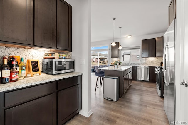 52690 Char Marie, Macomb, MI 48042 - kitchen featuring appliances with stainless steel finishes, dark brown cabinets, tasteful backsplash, light wood-style floors, and a breakfast bar