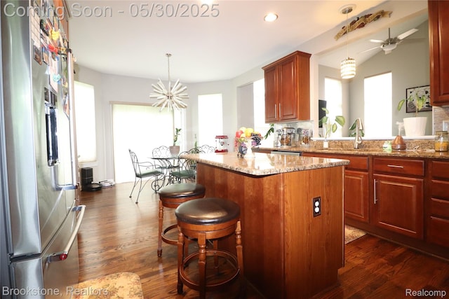 13961 Cobblestone Creek Dr, Belleville, MI 48111 - kitchen with a center island, dark wood-style flooring, light stone counters, a ceiling fan, and stainless steel fridge with ice dispenser