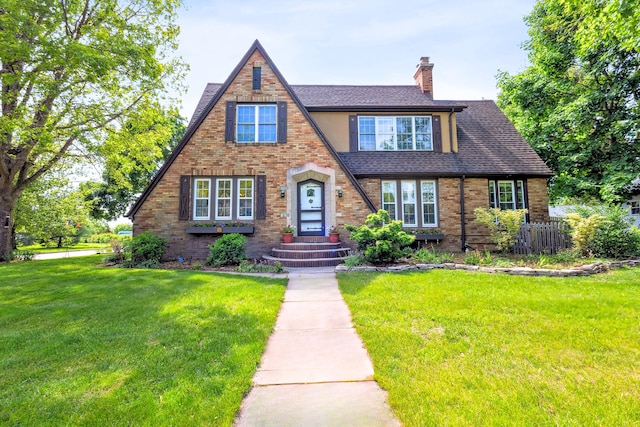 616 S Elm St, Three Oaks, MI 49128 - tudor home with a chimney, a front lawn, roof with shingles, and brick siding
