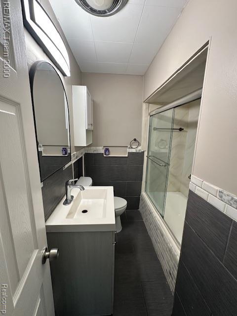 1042 Drexel St, Dearborn, MI 48128 - bathroom with vanity, shower / bath combination with glass door, toilet, tile walls, and wainscoting