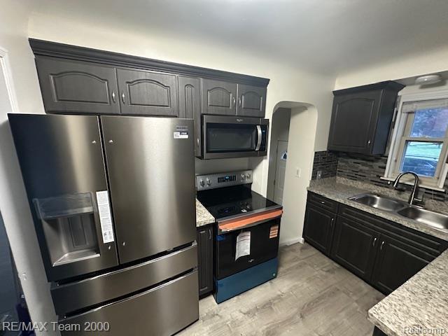 1042 Drexel St, Dearborn, MI 48128 - kitchen featuring stainless steel appliances, a sink, arched walkways, light wood-style flooring, and backsplash
