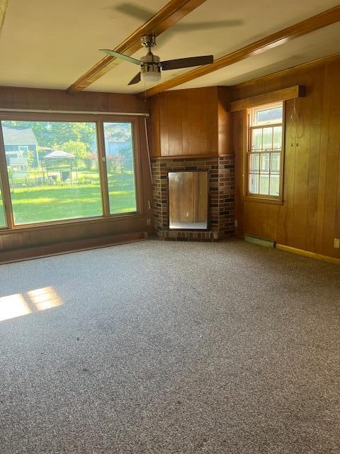 337 E Pine St, Fremont, MI 49412 - unfurnished living room featuring ceiling fan, a brick fireplace, beamed ceiling, wood walls, and carpet floors