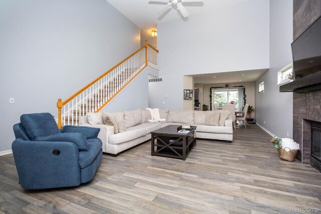 6075 Davison Rd, Burton, MI 48509 - living room featuring wood finished floors, stairway, a tiled fireplace, a ceiling fan, and a high ceiling