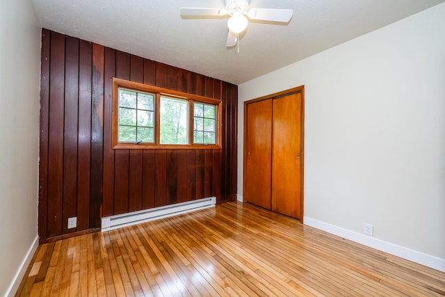 2800 Mayflower Rd, Niles, MI 49120 - unfurnished bedroom featuring a baseboard radiator, light wood finished floors, a closet, baseboards, and wood walls