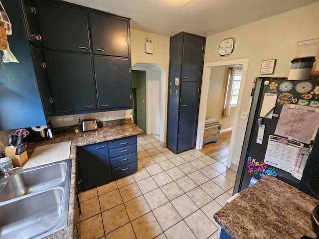 527 Jones St, Grand Ledge, MI 48837 - kitchen featuring a sink, freestanding refrigerator, arched walkways, light tile patterned floors, and dark countertops