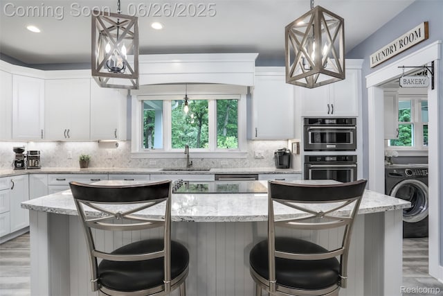 800 Greystone Dr, Chelsea, MI 48118 - kitchen featuring washer / clothes dryer, light wood-type flooring, white cabinetry, a center island, and backsplash