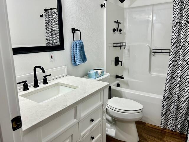 2985 Middle Lake Rd, Twin Lake, MI 49457 - full bath featuring vanity, toilet, shower / bathtub combination with curtain, and wood finished floors