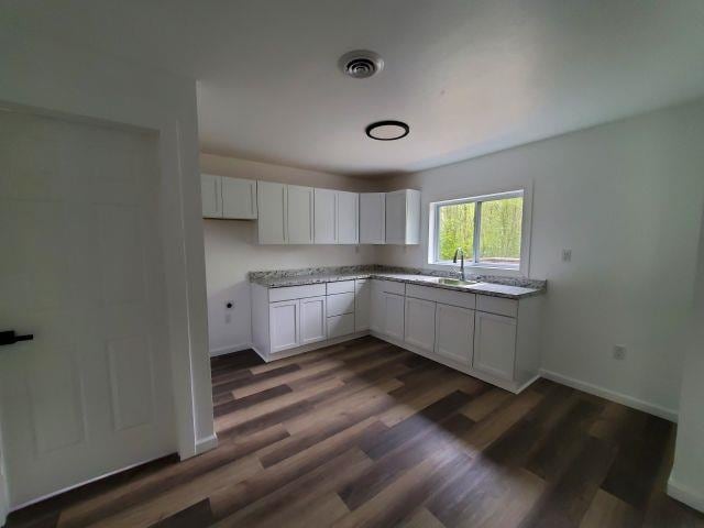 2153 Flowage Lake Rd, West Branch, MI 48661 - kitchen with dark wood-type flooring, white cabinets, a sink, and baseboards