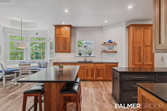 7149 Armadale Ct NE, Belmont, MI 49306 - kitchen with a sink, dark countertops, light wood finished floors, a breakfast bar area, and brown cabinetry