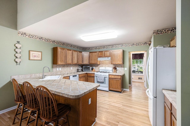 3311 Hickory Dr, Lake Orion, MI 48359 - kitchen featuring white appliances, under cabinet range hood, a peninsula, a breakfast bar, and tasteful backsplash