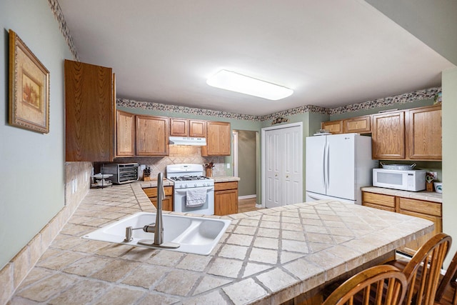 3311 Hickory Dr, Lake Orion, MI 48359 - kitchen with white appliances, under cabinet range hood, a sink, tile counters, and a peninsula