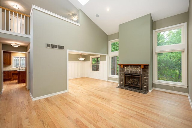 4936 Ravine Ct, Ann Arbor, MI 48105 - unfurnished living room featuring high vaulted ceiling, light wood-type flooring, plenty of natural light, a tile fireplace, and a skylight