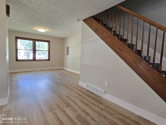 532 Grover St, Owosso, MI 48867 - unfurnished living room with a textured ceiling, wood finished floors, electric panel, baseboards, and stairway