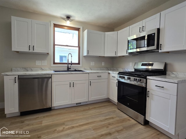 532 Grover St, Owosso, MI 48867 - kitchen with appliances with stainless steel finishes, a sink, white cabinetry, light wood-style flooring, and light countertops