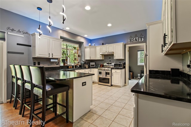 16429 E Horseshoe Trl, Linden, MI 48451 - kitchen with appliances with stainless steel finishes, a peninsula, under cabinet range hood, dark countertops, and a kitchen bar