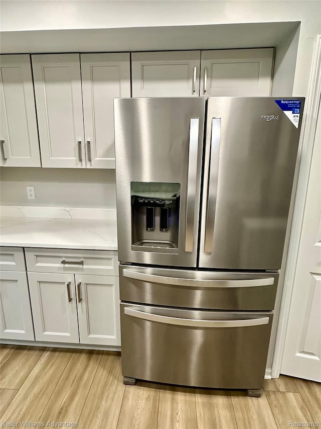 31404 Hunters Circle Dr, Farmington, MI 48334 - detailed view of stainless steel refrigerator with ice dispenser, light wood-type flooring, white cabinetry, and light stone countertops