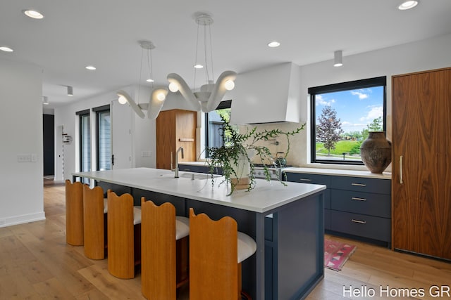 421 Manhattan Rd SE, Grand Rapids, MI 49506 - kitchen featuring light wood-type flooring, light countertops, a center island with sink, decorative light fixtures, and a kitchen breakfast bar