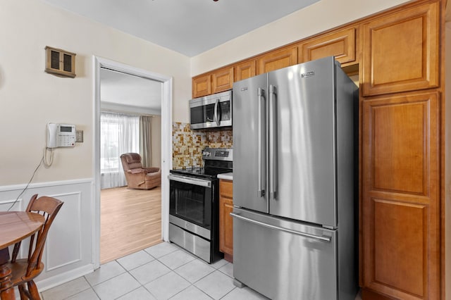 9085 Brentwood St, Livonia, MI 48150 - kitchen with stainless steel appliances, brown cabinets, light tile patterned flooring, wainscoting, and tasteful backsplash