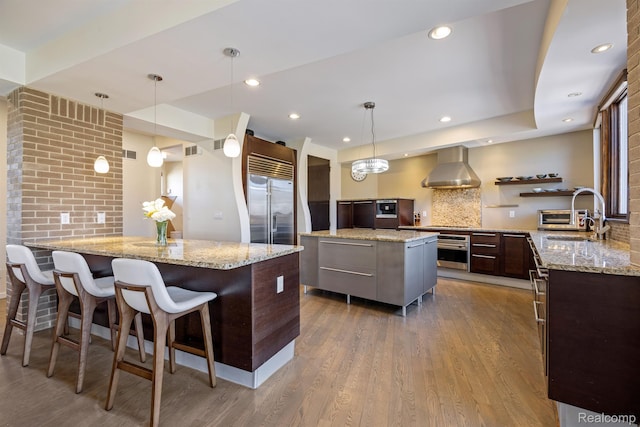 1000 Forest Ln, Bloomfield Hills, MI 48301 - kitchen with wall chimney range hood, stainless steel appliances, a kitchen island, a sink, and dark wood finished floors
