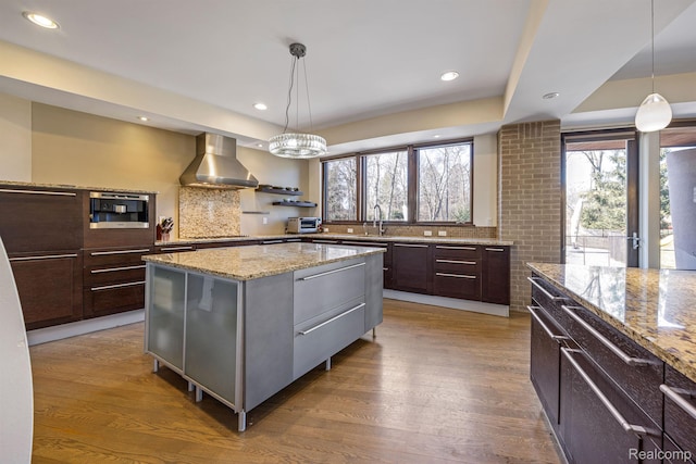 1000 Forest Ln, Bloomfield Hills, MI 48301 - kitchen featuring wall chimney exhaust hood, wood finished floors, light stone countertops, a center island, and dark brown cabinetry