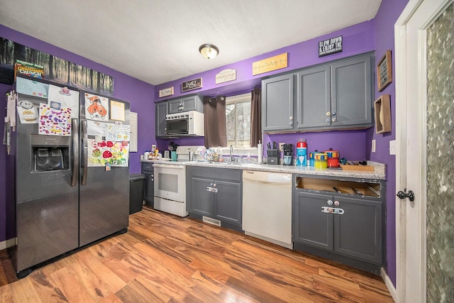 114 Orange St, Jackson, MI 49202 - kitchen with white appliances, wood finished floors, light countertops, gray cabinets, and a sink