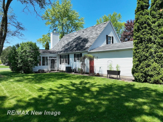 5475 George St, Saginaw, MI 48603 - rear view of property featuring a lawn, a chimney, a sunroom, cooling unit, and a shingled roof