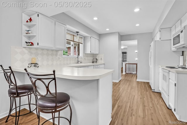 9587 Harmon Ln, South Lyon, MI 48178 - kitchen with white appliances, a peninsula, white cabinets, backsplash, and light wood finished floors