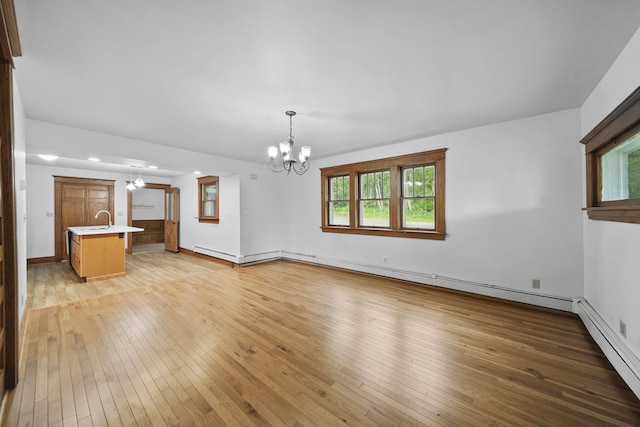 7331 Browns Lake Rd, Jackson, MI 49201 - unfurnished living room featuring a chandelier, light wood-style flooring, a baseboard heating unit, baseboard heating, and a sink