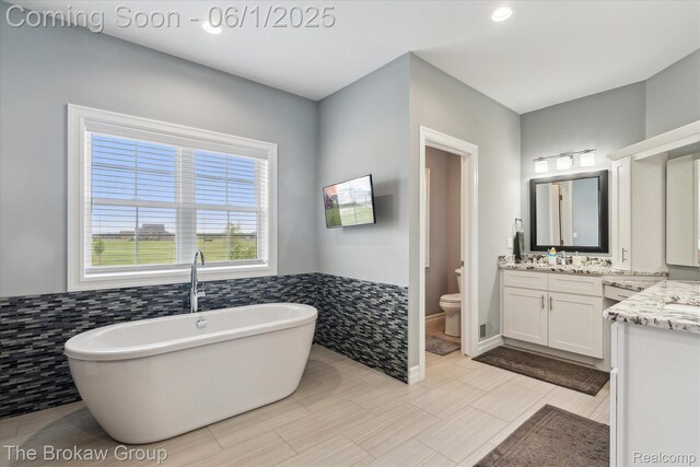 6268 Victoria Ln, Swartz Creek, MI 48473 - full bathroom with vanity, a freestanding tub, toilet, tile walls, and a wainscoted wall