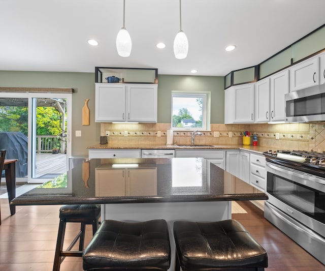702 Starfield Dr, Pinckney, MI 48169 - kitchen with stainless steel appliances, a sink, white cabinetry, a breakfast bar area, and decorative backsplash