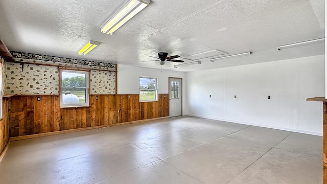 1972 W Cedar Dr, Mcbain, MI 49657 - empty room featuring a textured ceiling, concrete flooring, plenty of natural light, wooden walls, and a wainscoted wall