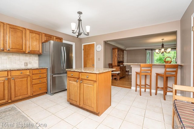 241 E Gunn Rd, Rochester, MI 48306 - kitchen with a chandelier, freestanding refrigerator, backsplash, a center island, and brown cabinets