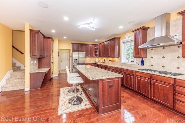 15390 Prestwick Cir, Northville, MI 48168 - kitchen featuring wall chimney range hood, appliances with stainless steel finishes, dark wood-style flooring, a center island, and recessed lighting