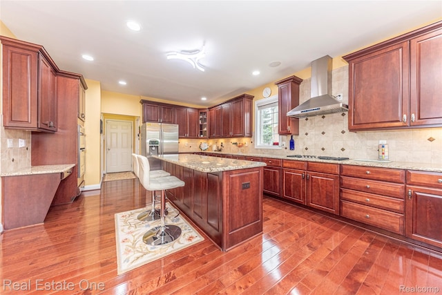 15390 Prestwick Cir, Northville, MI 48168 - kitchen featuring wall chimney range hood, dark wood-style flooring, stainless steel appliances, a breakfast bar, and a kitchen island