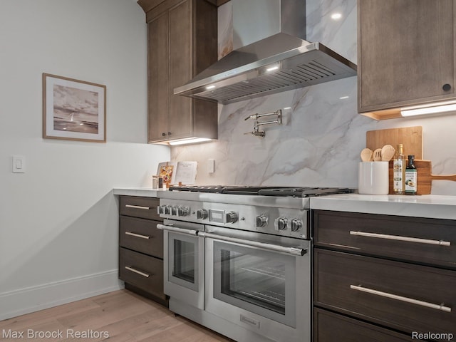 667 Oak Ave, Birmingham, MI 48009 - kitchen featuring double oven range, wall chimney range hood, decorative backsplash, light countertops, and light wood-style floors