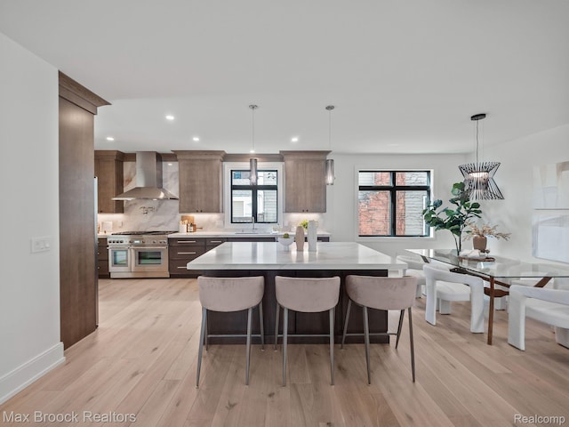 667 Oak Ave, Birmingham, MI 48009 - kitchen with range with two ovens, wall chimney exhaust hood, light wood-style flooring, light countertops, and backsplash