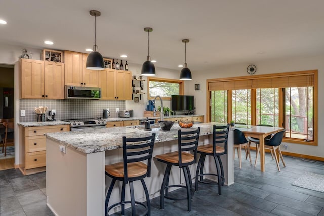 7346 Dunross Dr, Portage, MI 49024 - kitchen with appliances with stainless steel finishes, light brown cabinetry, a kitchen island with sink, decorative backsplash, and a kitchen bar
