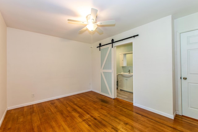 4225 Central Blvd, Ann Arbor, MI 48108 - unfurnished bedroom featuring a barn door, wood finished floors, baseboards, a sink, and connected bathroom