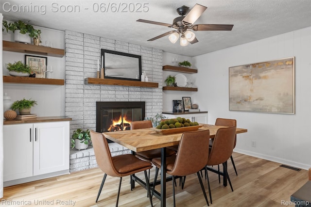 569 Lyon Blvd, South Lyon, MI 48178 - dining room with a fireplace, a textured ceiling, light wood-style flooring, a ceiling fan, and baseboards