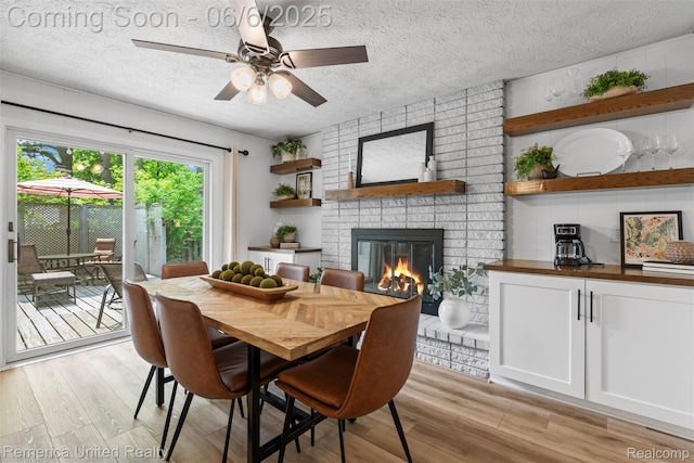 569 Lyon Blvd, South Lyon, MI 48178 - dining room featuring a brick fireplace, a textured ceiling, ceiling fan, and light wood finished floors
