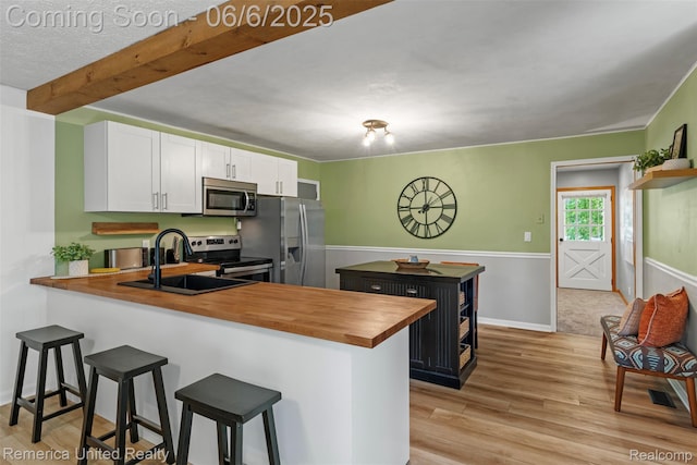 569 Lyon Blvd, South Lyon, MI 48178 - kitchen featuring wooden counters, stainless steel appliances, white cabinets, a breakfast bar area, and light wood-style flooring