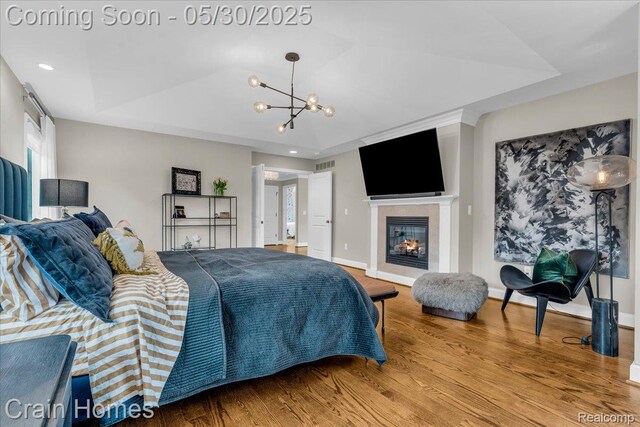 499 Catalpa Dr, Birmingham, MI 48009 - bedroom with wood finished floors, a chandelier, a tray ceiling, baseboards, and a glass covered fireplace