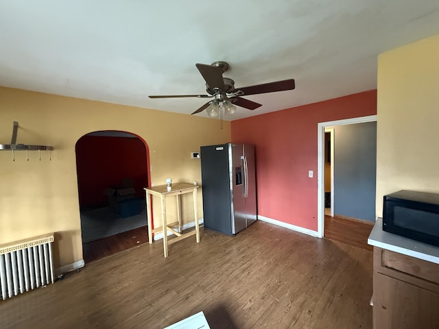 21338 Orchard Lake Rd, Farmington Hills, MI 48336 - unfurnished living room with radiator, arched walkways, a ceiling fan, wood finished floors, and baseboards