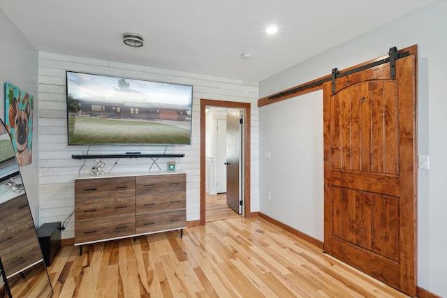 10200 Jerome Rd N, Jerome, MI 49249 - unfurnished bedroom featuring light wood finished floors, baseboards, wooden walls, a barn door, and recessed lighting
