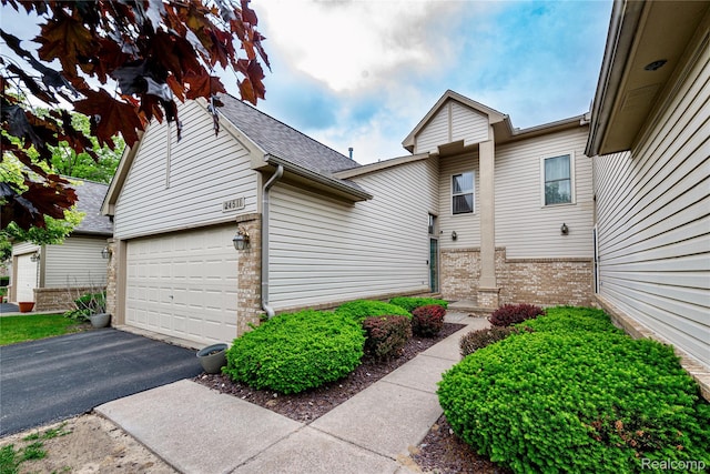 24511 Pinehurst Ave Unit 14, Oak Park, MI 48237 - view of exterior entry with brick siding, driveway, a garage, and a shingled roof