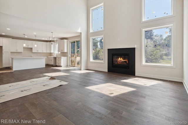 2911 Walsh Dr, Rochester Hills, MI 48309 - unfurnished living room with a towering ceiling, a glass covered fireplace, baseboards, a sink, and wood finished floors