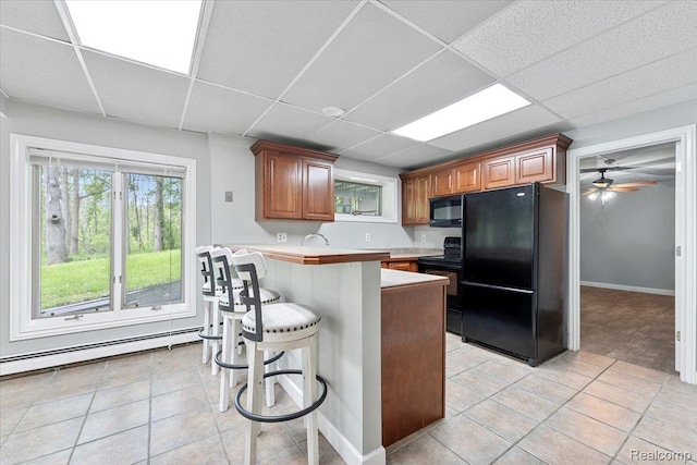 10161 N Loma Cir, Grosse Ile, MI 48138 - kitchen with black appliances, light tile patterned floors, light countertops, a baseboard heating unit, and a drop ceiling